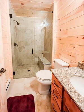 A bathroom with a glass-enclosed shower, a white toilet, and a wooden vanity with a marble countertop.