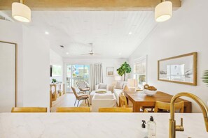 A modern kitchen with a marble countertop, a gold faucet, and a dining area with a wooden table and chairs.