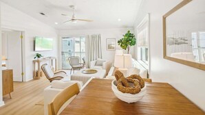 A modern living room with a wooden dining table, white sofas, a ceiling fan, and a large window with curtains. - Grayt Days by Stay on 30a (Santa Rosa Beach)