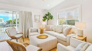 A bright living room with a ceiling fan, large windows, a white sofa set, a wicker chair, and a side table with a lamp. - Grayt Days by Stay on 30a (Santa Rosa Beach)