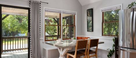 A kitchen with a dining table, chairs, a refrigerator, and large windows with a view of greenery.