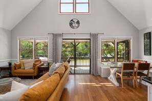 Un salon spacieux avec un plafond haut, de grandes fenêtres, un plancher en bois et un coin salon confortable avec un canapé et des fauteuils.