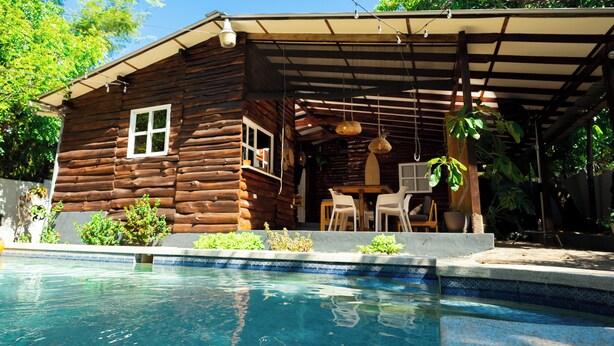 A wooden cabin with a pool, outdoor seating, and a covered patio area.