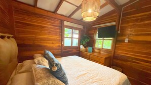A wooden cabin bedroom with a bed, pillows, a dresser, and a hanging plant.