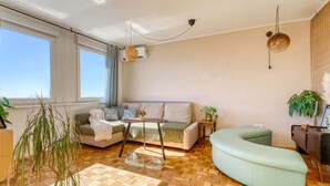 Un salon moderne avec un canapé aux lignes courbes, un parquet en bois disposé en chevrons, une petite table et une plante en pot.