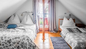 A cozy attic bedroom with two beds, a wooden floor, and a window with curtains.