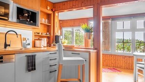 A modern kitchen with wooden cabinetry, a built-in dishwasher, and a large window offering a view of greenery outside.
