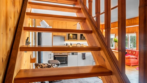 A wooden staircase leading to a living area with a kitchen and a red sofa.