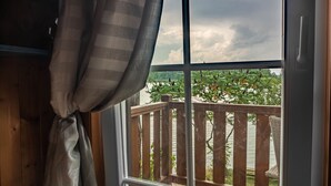 A room with a wooden window frame, a view of a wooden deck, and a balcony with a railing.