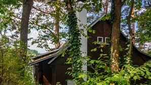A rustic wooden cabin surrounded by dense foliage, with a wooden staircase leading to a door.