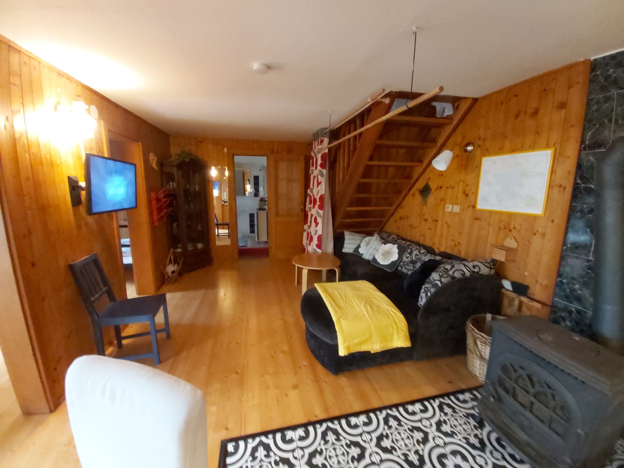 A cozy living room with a wooden interior, a television, a sofa, a chair, a fireplace, and a staircase.