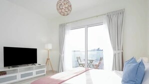 Camera d'albergo con un letto grande, una TV a schermo piatto, un balcone con tavolo e sedie e un'ampia finestra con tende.