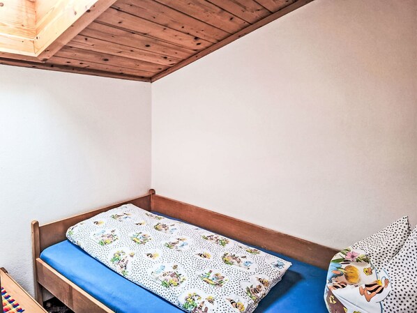 A small, single-bed room with a wooden headboard, a blue mattress, and a white wall with a wooden ceiling.