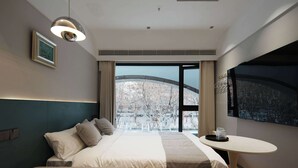 A hotel room with a bed, bedside table, and a large window offering a view of trees and buildings. - Colorstory Hotel (Hangzhou)