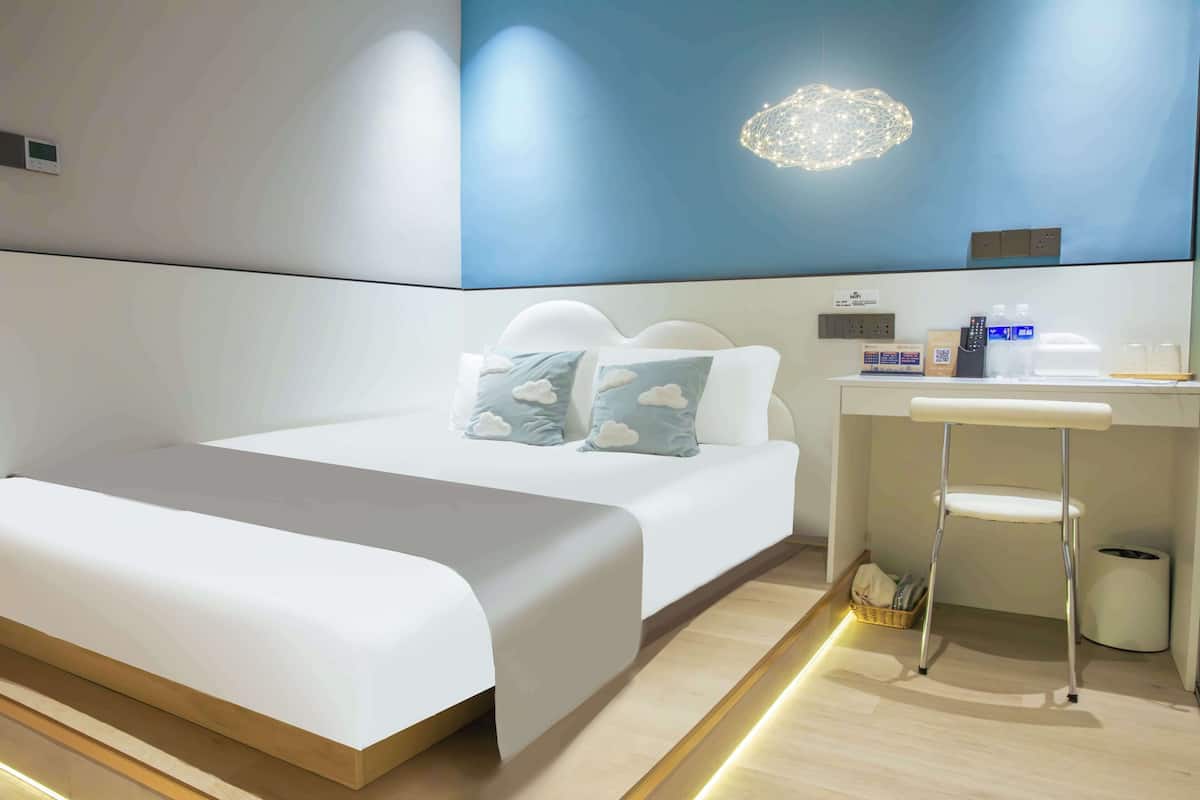 A modern hotel room with a large bed, a desk, and a wall-mounted light fixture.