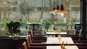 An indoor dining area with tables and chairs, a hanging light fixture, and a view of trees and buildings outside. - Colorstory Hotel (Hangzhou)