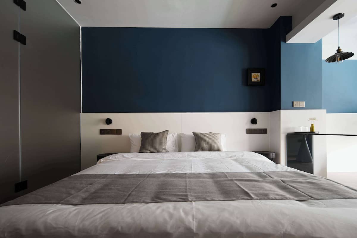 A modern bedroom with a large bed, a dark accent wall, and a bedside table with a lamp.