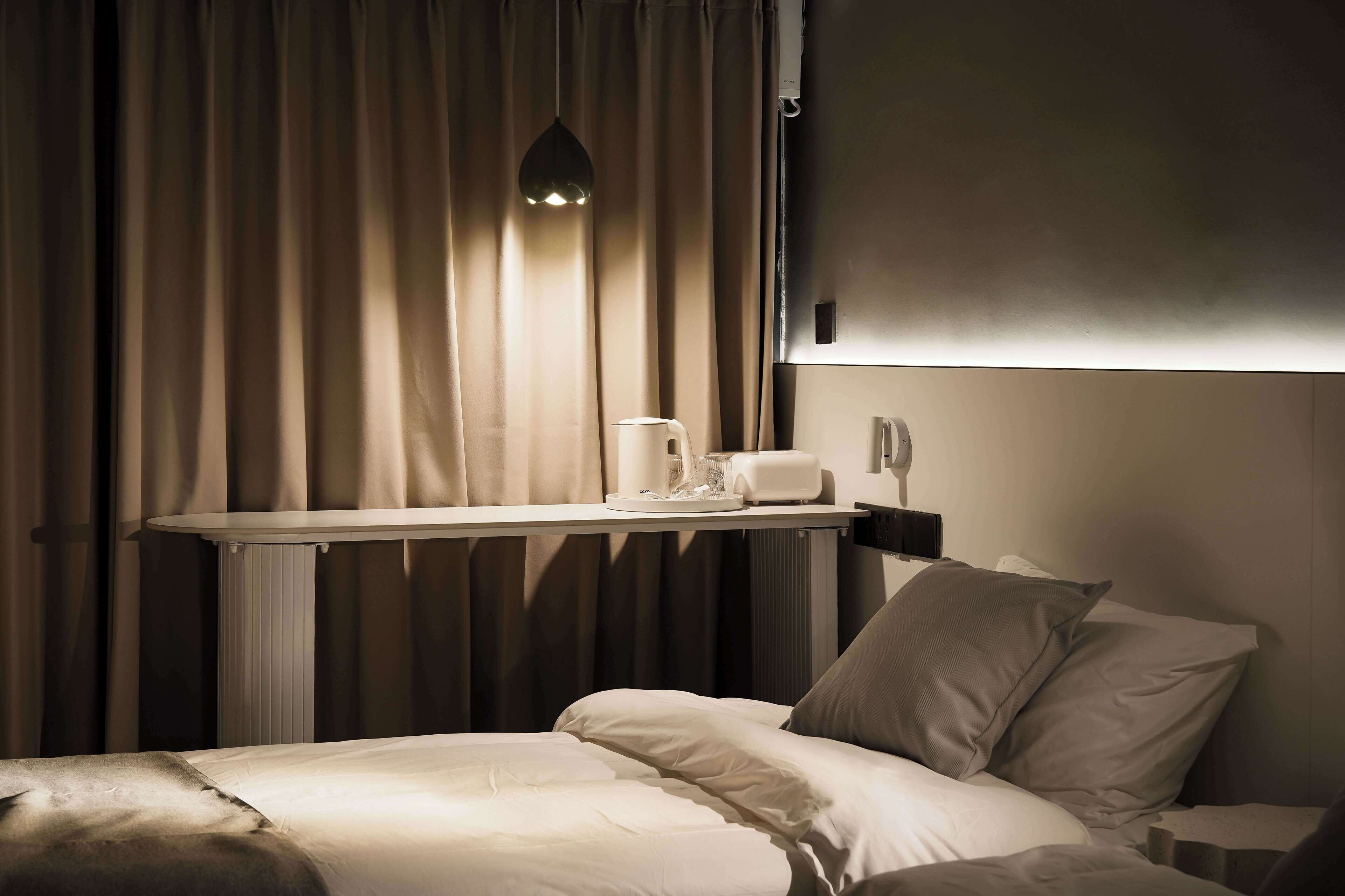 Een hotelkamer met een bed, een nachtkastje met een lamp, een koffiezetapparaat en gordijnen.
