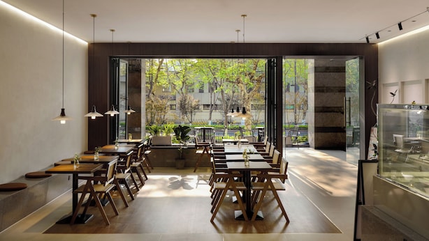 A modern restaurant with wooden tables and chairs, large windows offering a view of the outdoors, and pendant lighting. - Colorstory Hotel (Hangzhou)