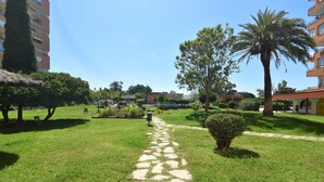 A pathway leading through a well-maintained garden with a palm tree and a thatched-roof structure. - Discover this charming studio in Santa Margarita, Roses! (Roses)