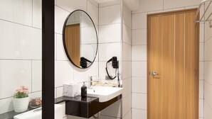 A modern bathroom with a wooden door, a round mirror, a white sink, and a black countertop. - Infinite Hotel Kaset-Senanikom (Bangkok)