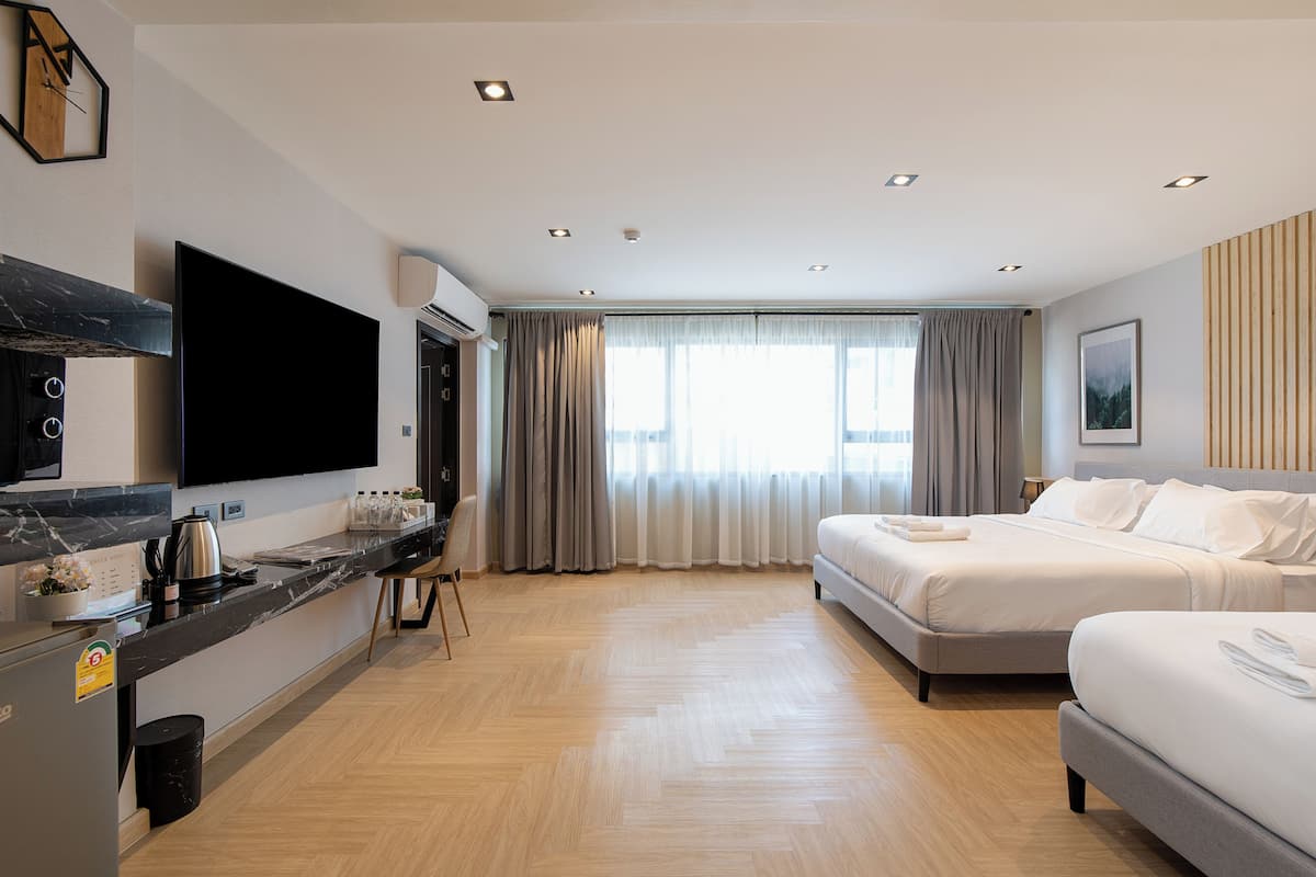 Een moderne hotelkamer met een groot bed, een bureau met een flatscreen-televisie, een kitchenette en een groot raam met gordijnen.