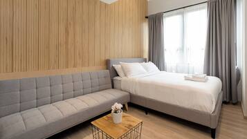 A modern hotel room with a sofa, a bed, and a wooden accent wall.