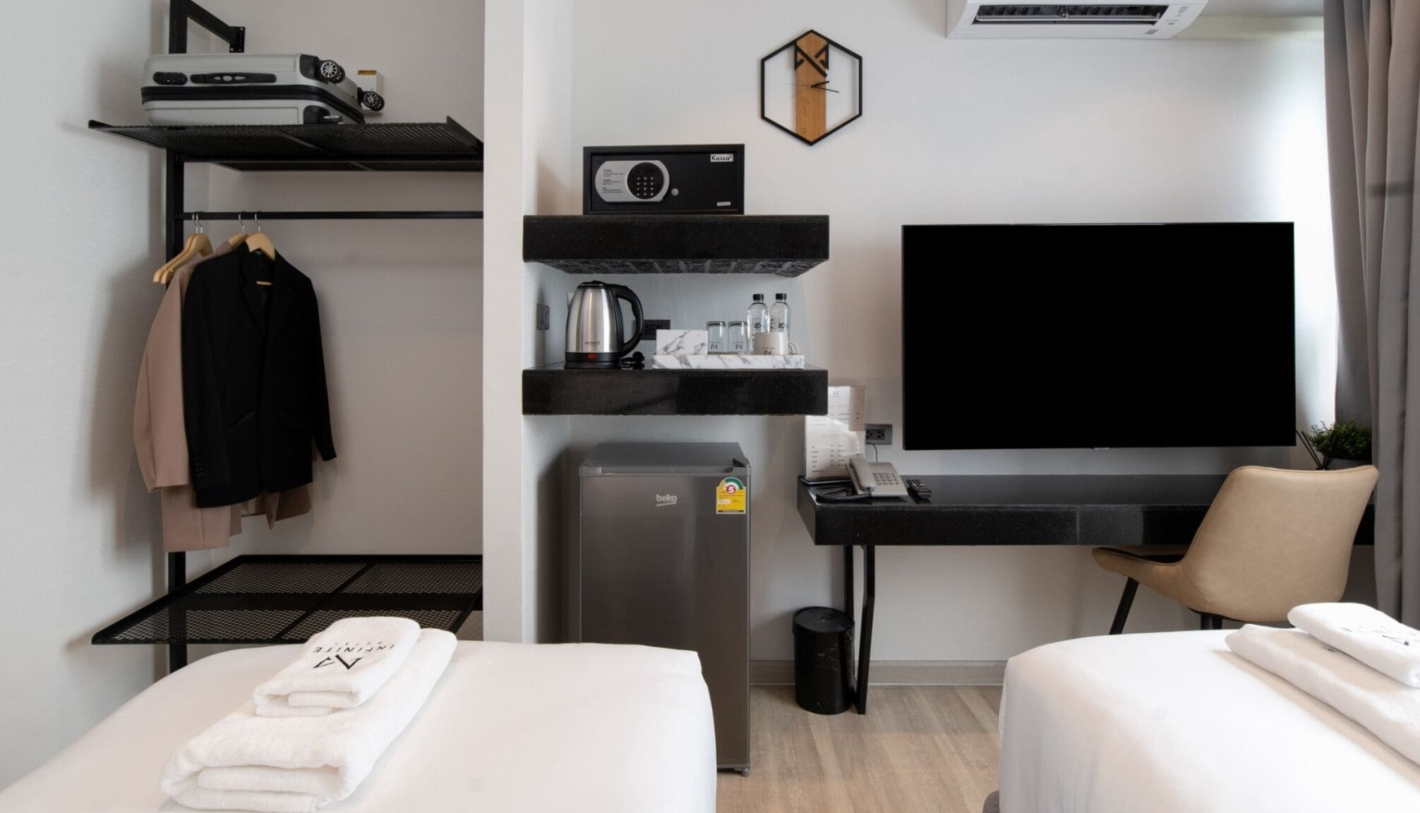 A hotel room with two beds, a desk with a flat-screen TV, a minibar, a coffee machine, and a small refrigerator.
