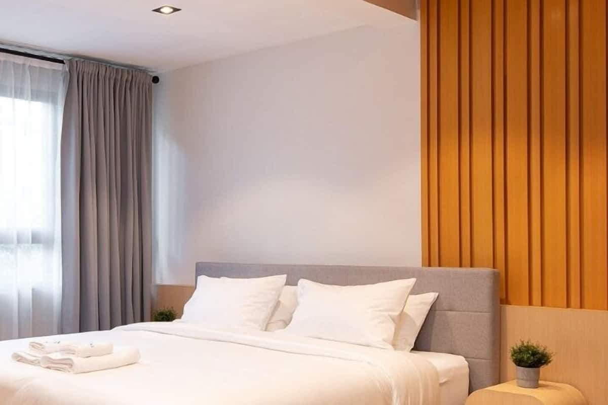 Een moderne slaapkamer met een grijs bed, witte lakens, een houten hoofdbord en een klein nachtkastje met een plant.