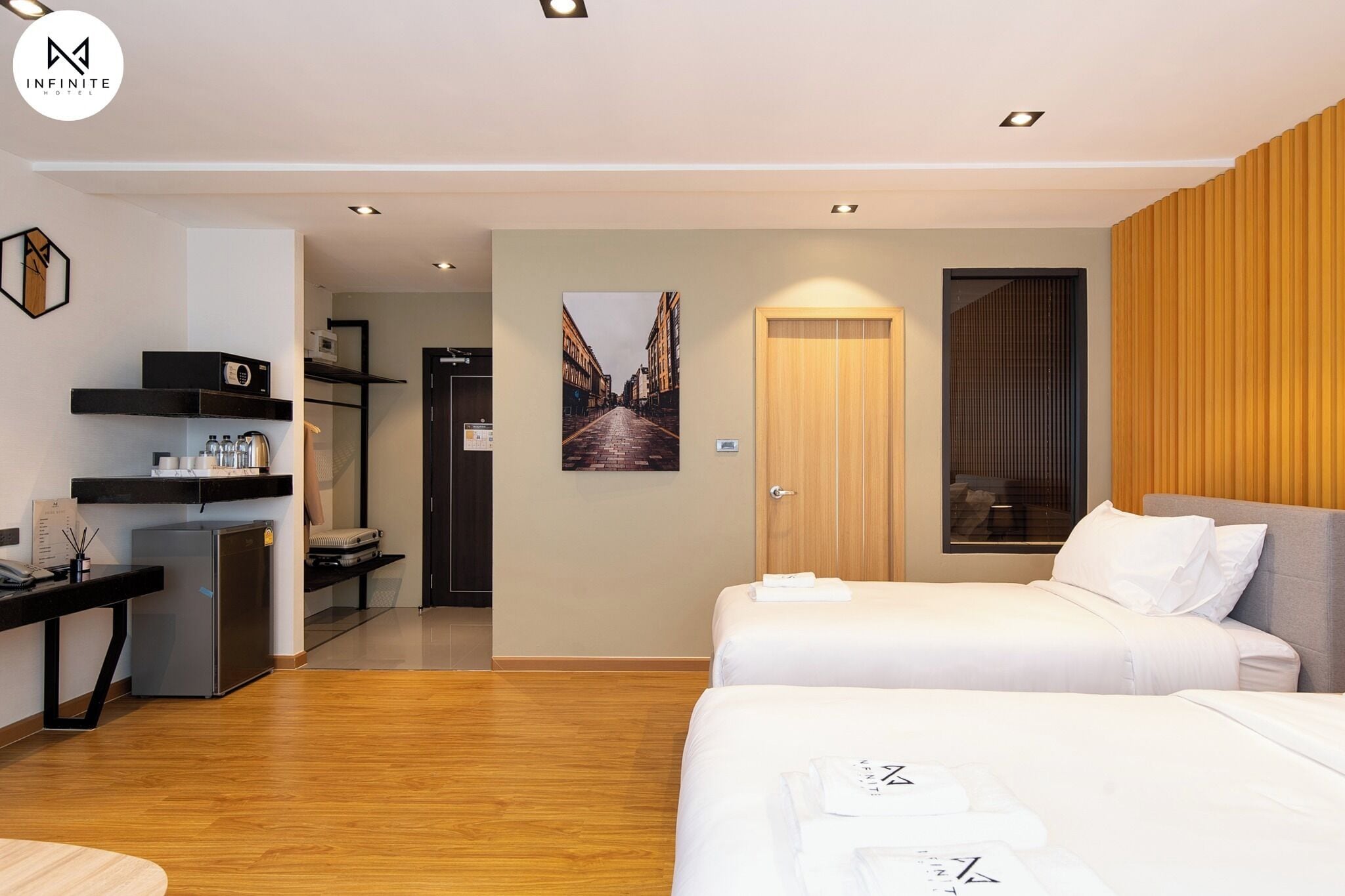 Ein modernes Hotelzimmer mit zwei Betten, einem Schreibtisch mit Kühlschrank, einer Wandpaneele aus Holz und einem Stadtbild an der Wand.