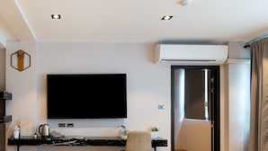 A modern living room with a large flat-screen TV, a black marble countertop, a wooden herringbone floor, and a sliding glass door leading to a balcony. - Infinite Hotel Kaset-Senanikom (Bangkok)