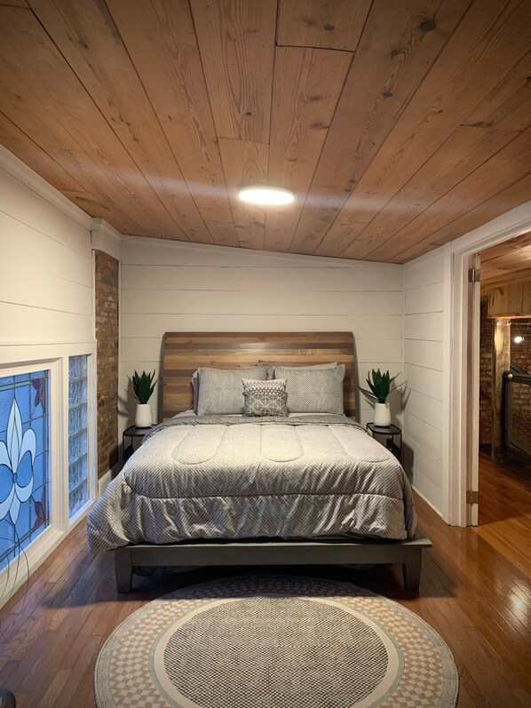 Ein Schlafzimmer mit Holzbalkendecke, einem Bett mit gemusterten Textilien, zwei Nachttischen mit Pflanzen und einem dekorativen Teppich.