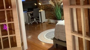 A cozy room with a wooden ceiling, a desk with a chair, a bed with a patterned rug, and a potted plant. - Supercool 2-Bedroom Modern Rustic Loft in Downtown Eatonton, Near Lake Oconee (Eatonton)