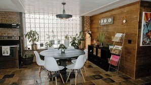 A dining area with a round table, white chairs, and potted plants. There is a brick wall, a window with a grid pattern, and a clock on the wall. - Supercool 2-Bedroom Modern Rustic Loft in Downtown Eatonton, Near Lake Oconee (Eatonton)