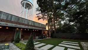 A rustic building with a water tower in the background, a covered patio with string lights, and a well-maintained lawn. - Supercool 2-Bedroom Modern Rustic Loft in Downtown Eatonton, Near Lake Oconee (Eatonton)