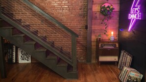 A staircase with a metal railing, a neon sign that says "Let's Dance", a small table with a plant, and a rack of vinyl records. - Supercool 2-Bedroom Modern Rustic Loft in Downtown Eatonton, Near Lake Oconee (Eatonton)