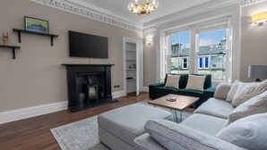 A living room with a fireplace, a sofa, a coffee table, and a TV mounted on the wall. - GuestReady - Bright & Modern 2BR in Edinburgh (Edinburgh)