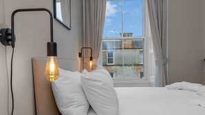 A neatly made bed with white linens, two bedside lamps, and a window with curtains. - GuestReady - Bright & Modern 2BR in Edinburgh (Edinburgh)