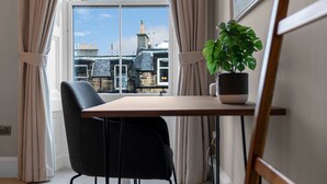 A room with a view of buildings through a window, a table with a plant, and a chair. - GuestReady - Bright & Modern 2BR in Edinburgh (Edinburgh)