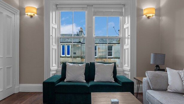 A living room with a green sofa, a grey sofa, and a wooden coffee table. There are two wall-mounted lamps and a lamp on a side table. - GuestReady - Bright & Modern 2BR in Edinburgh (Edinburgh)