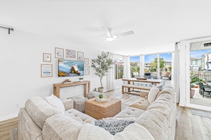 A living room with a sofa, a TV, a ceiling fan, and a view of the outdoors.