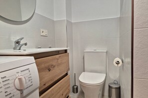 Een moderne badkamer met een wit toilet, een wastafel met kraan, een spiegel en een houten wastafelmeubel.