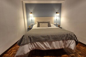 A narrow room with a bed, two bedside lamps, a patterned pillow, and a striped bedspread.