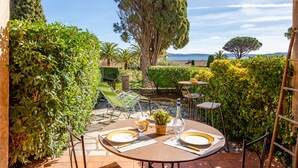 A patio with a table set for two, surrounded by greenery and a view of the sea. - El Cantarello by Interhome (Sainte Maxime)