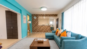 A modern living room with a sofa, coffee table, and a dining area with a wooden floor and a herringbone-patterned wall. - Premier Villa Miyako (Miyakojima)