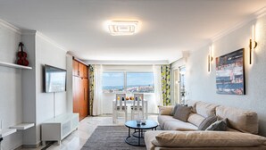 A modern living room with a sofa, a coffee table, and a TV. There is a window with a view of the city and a door leading to another room. - Marvelous views, pools, steps to the beach! REF024 (Benalmádena)