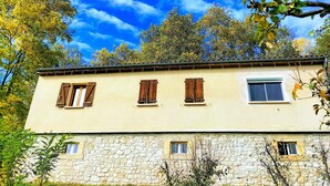 Un edificio de piedra de dos pisos con varias ventanas, rodeado de vegetación y árboles.