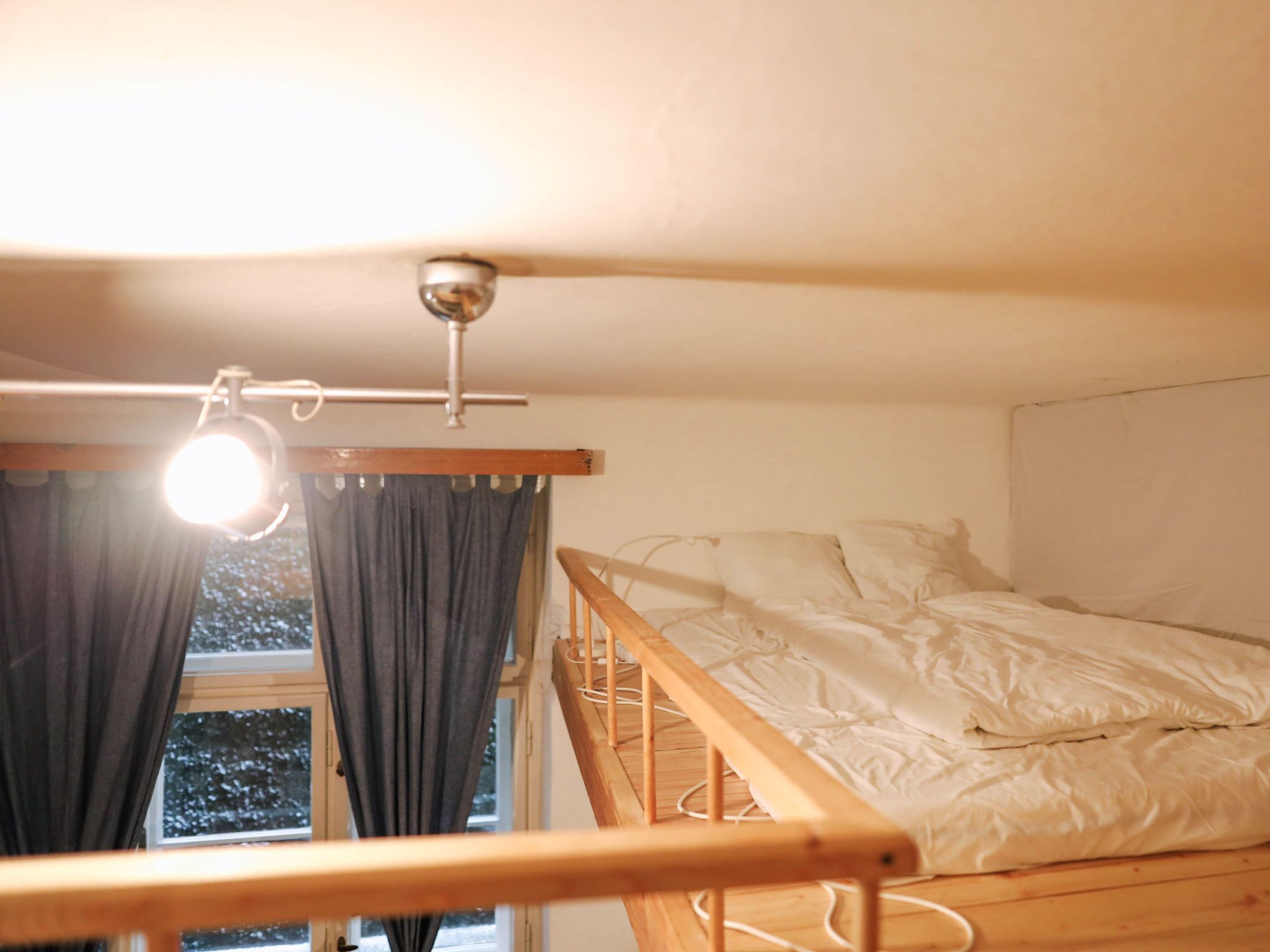 Una habitación pequeña con una cama individual y literas de madera, y una ventana con cortinas.