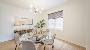 Un coin repas comprenant une table en verre, quatre chaises, un lustre, une fenêtre avec des stores et un élément décoratif mural.