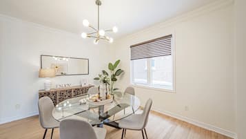 Un coin repas comprenant une table en verre, quatre chaises, un lustre, une fenêtre avec des stores et un élément décoratif mural.